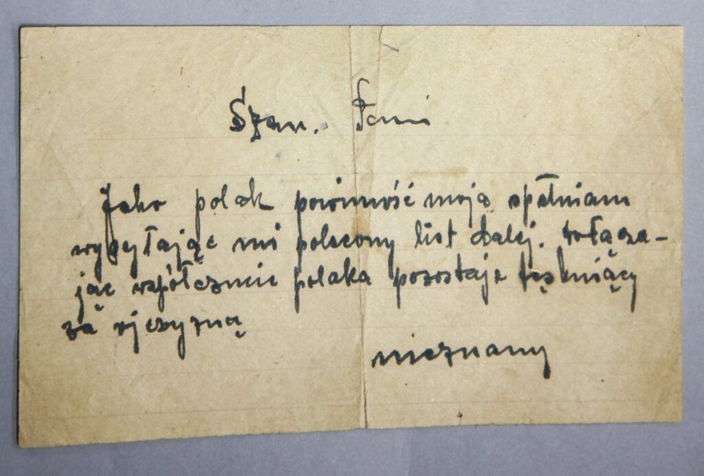 Ręcznie napisana notatka po polsku na starym, pożółkłym papierze, z tekstem napisanym czarnym atramentem. Zagięcia i wytarte krawędzie muzealium przywołują jego historię, zachowaną od 2020 r., na jednolitym szarym tle.