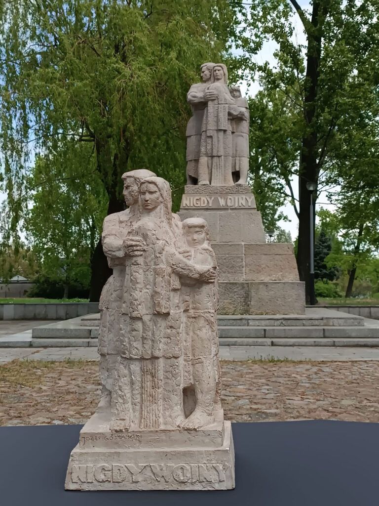 Niewielka rzeźba Józefa Gosławskiego przedstawiająca kobietę trzymającą dziecko stoi przed większą statuą, na obu z napisem „Nigdy wojny”. Umieszczona w parku z drzewami i kamiennym chodnikiem, może być częścią wystawy czasowej.
