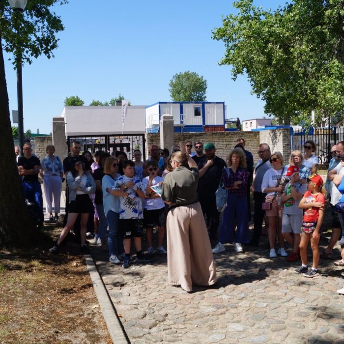 Grupa osób zwiedza teren dawnego niemieckiego obozu karno-śledczego w Muzeum Męczeństwa w Żabikowie z przewodnikiem.